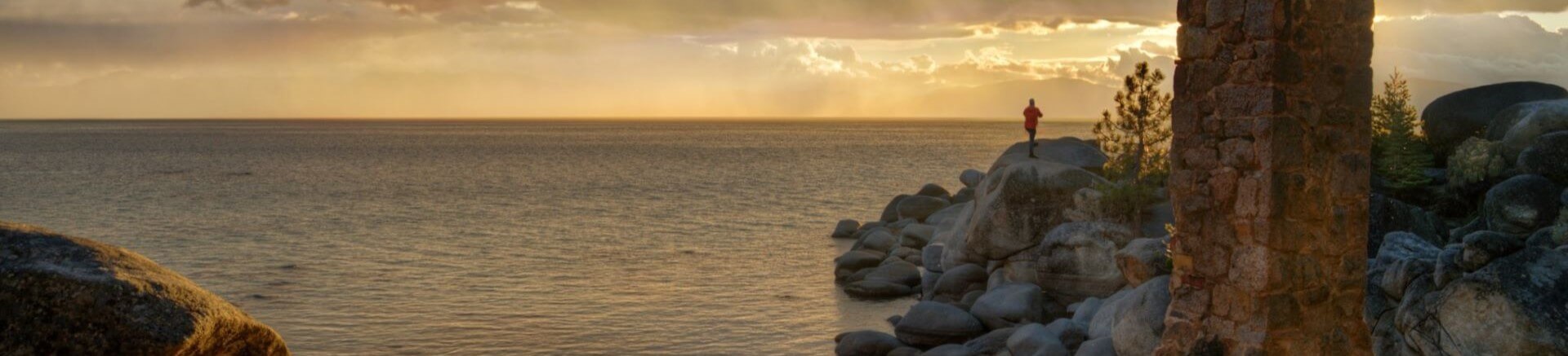 Scenic view of Lake Tahoe at sunset with a person standing on rocks