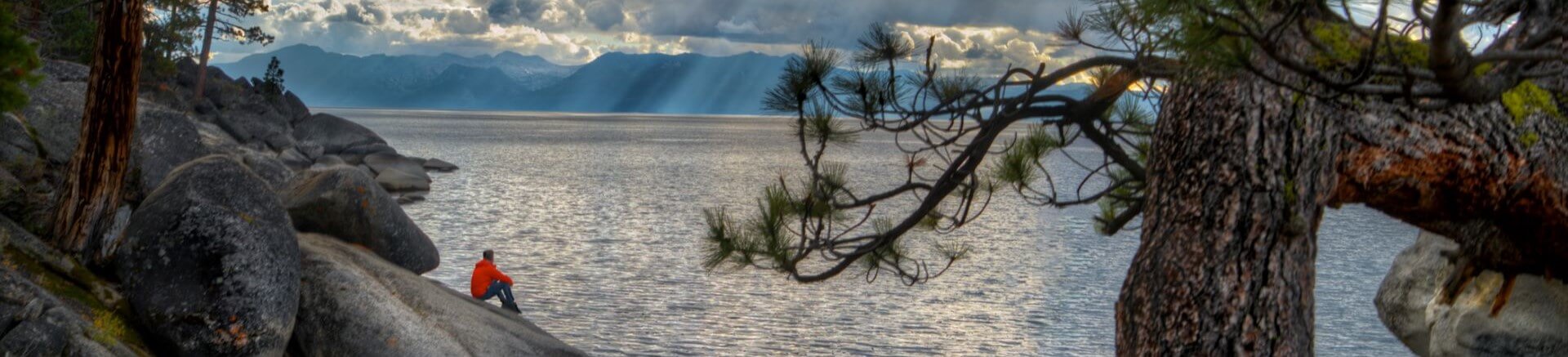 Scenic view of Lake Tahoe with mountains in the background and a person sitting on the rocks